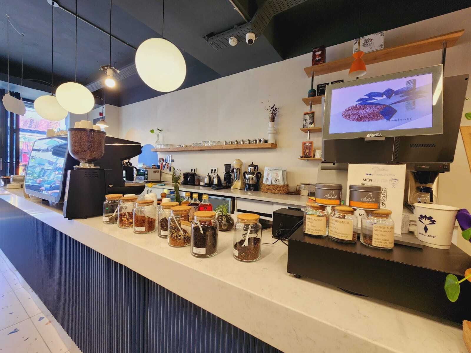 A coffee shop counter with a variety of coffee beans and jars, a coffee machine, and a television displaying a coffee advertisement.
