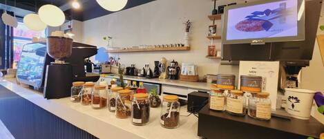 A coffee shop counter with a variety of coffee beans and jars, a coffee machine, and a television displaying a coffee advertisement.