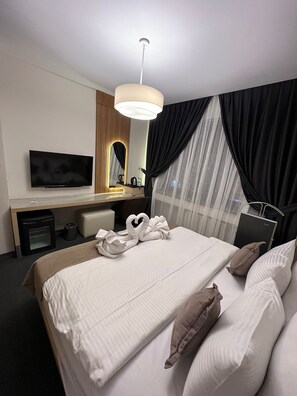 Une chambre d’hôtel avec un lit, un bureau équipé d’un ordinateur, une télévision et une fenêtre avec des rideaux noirs.