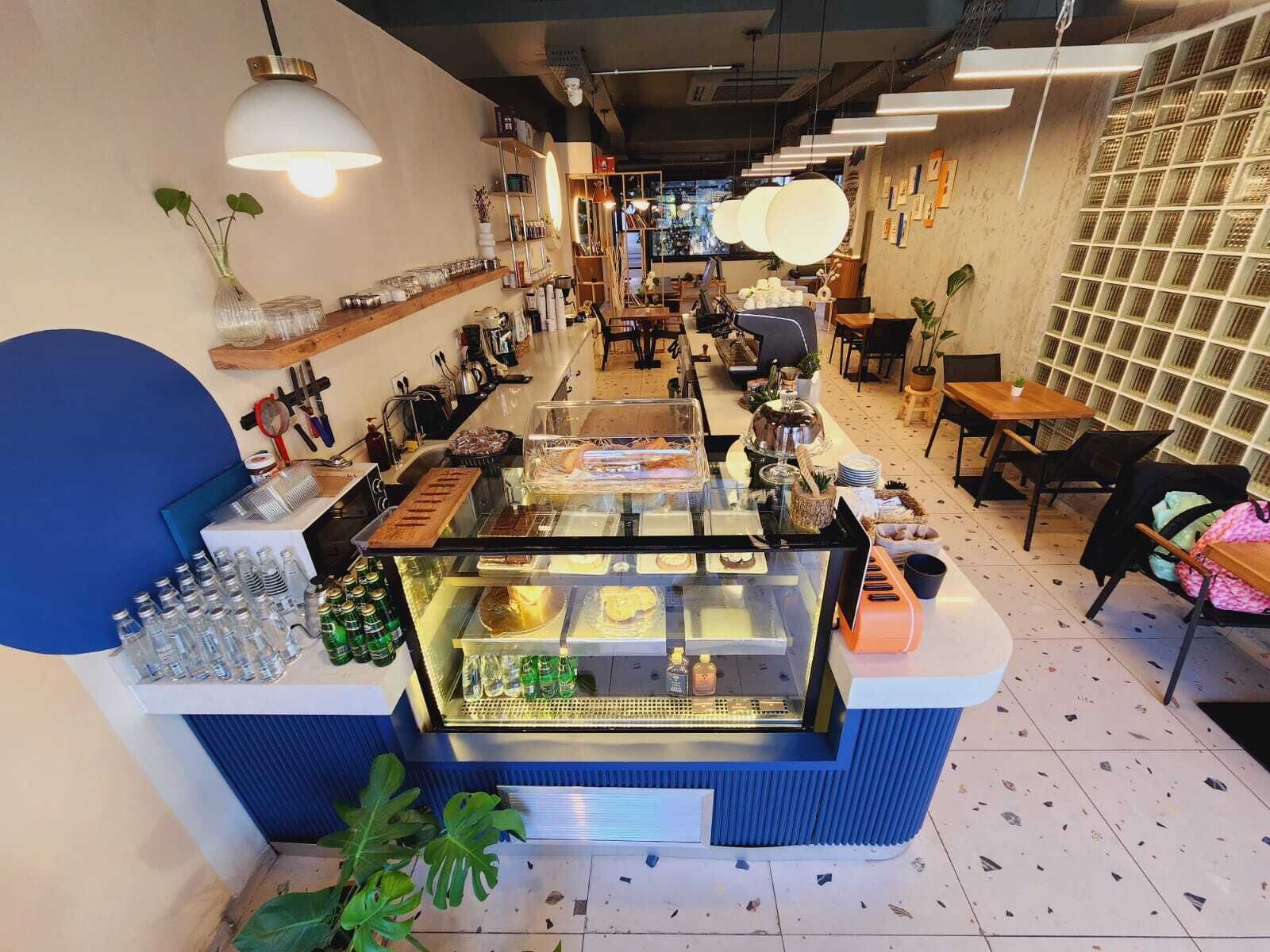 A café with a central counter displaying food items, shelves with various products, and seating areas.
