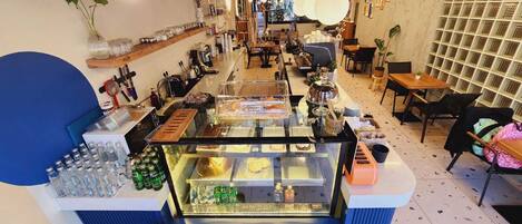 A café with a central counter displaying food items, shelves with various products, and seating areas.