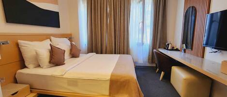 Habitación de hotel con cama, escritorio, silla, televisor y un amplio ventanal con cortinas.