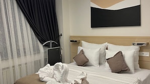 A hotel room with a bed, a hanging light fixture, a painting on the wall, and a window with curtains. - Mahall Hotel (Istanbul)