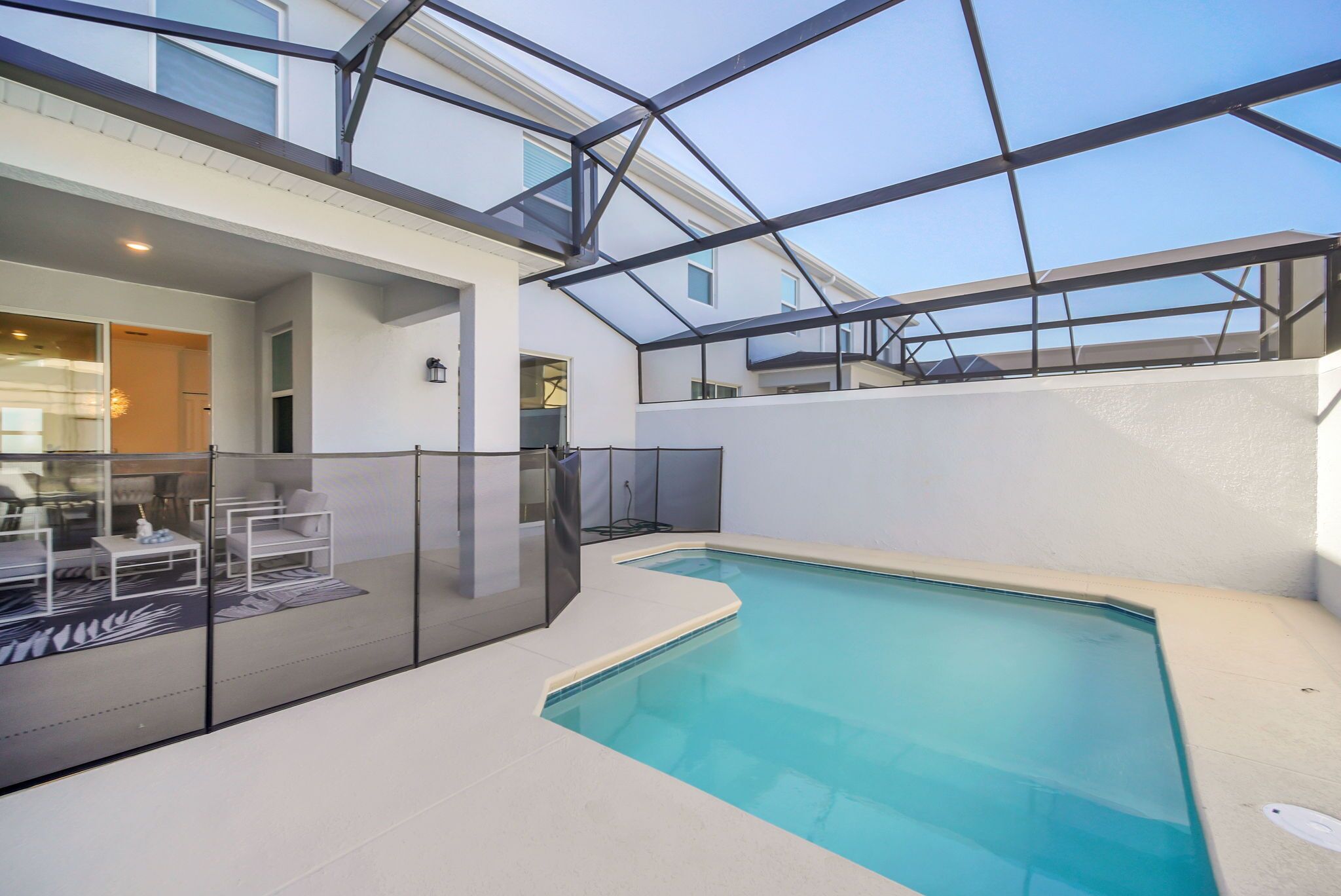 A modern indoor pool area with glass walls, a seating area with white furniture, and a clear view of the sky.