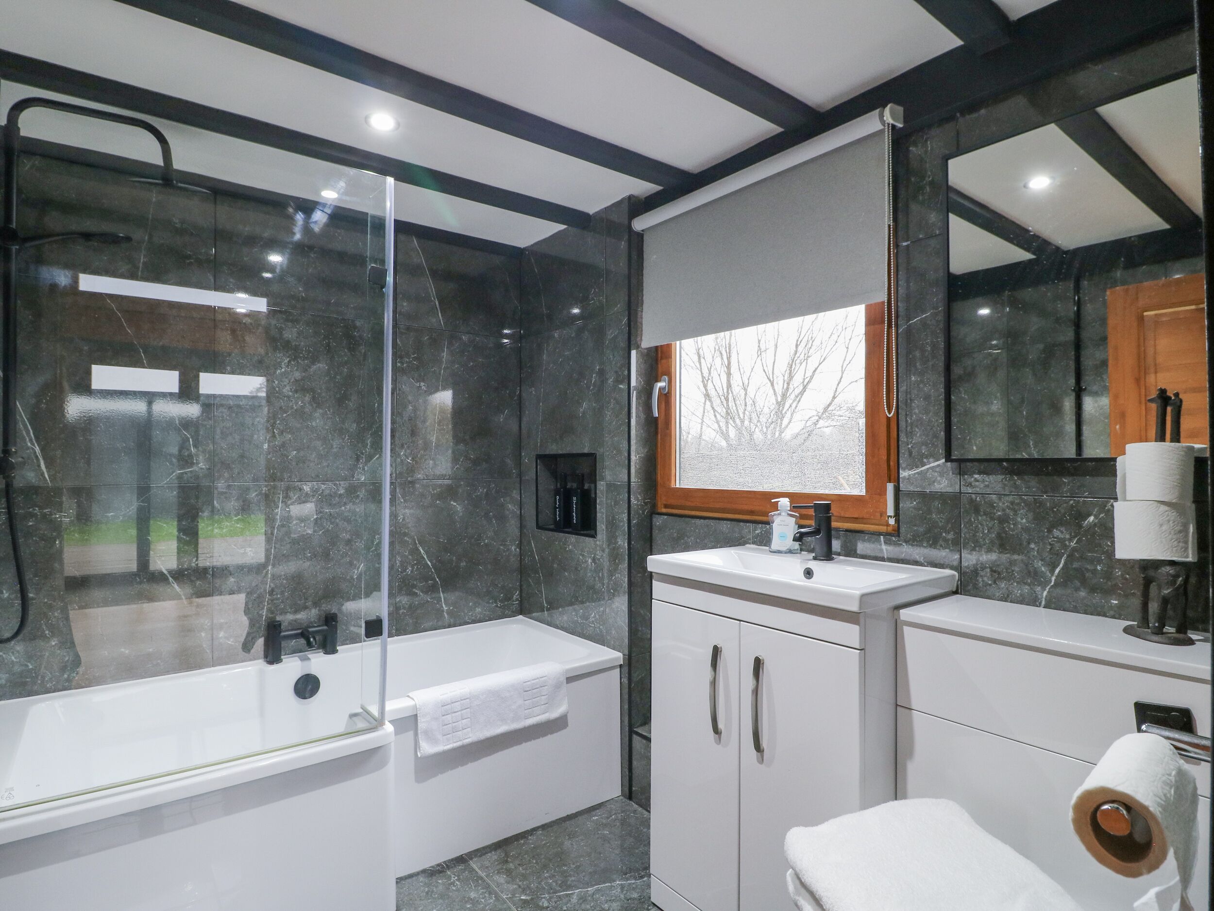 Un baño moderno con ducha de vidrio, un lavamanos blanco con un espejo encima y un inodoro con un perchero para toallas.