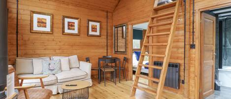 A cozy cabin interior with a wooden interior, a sofa, a table, and a ladder.