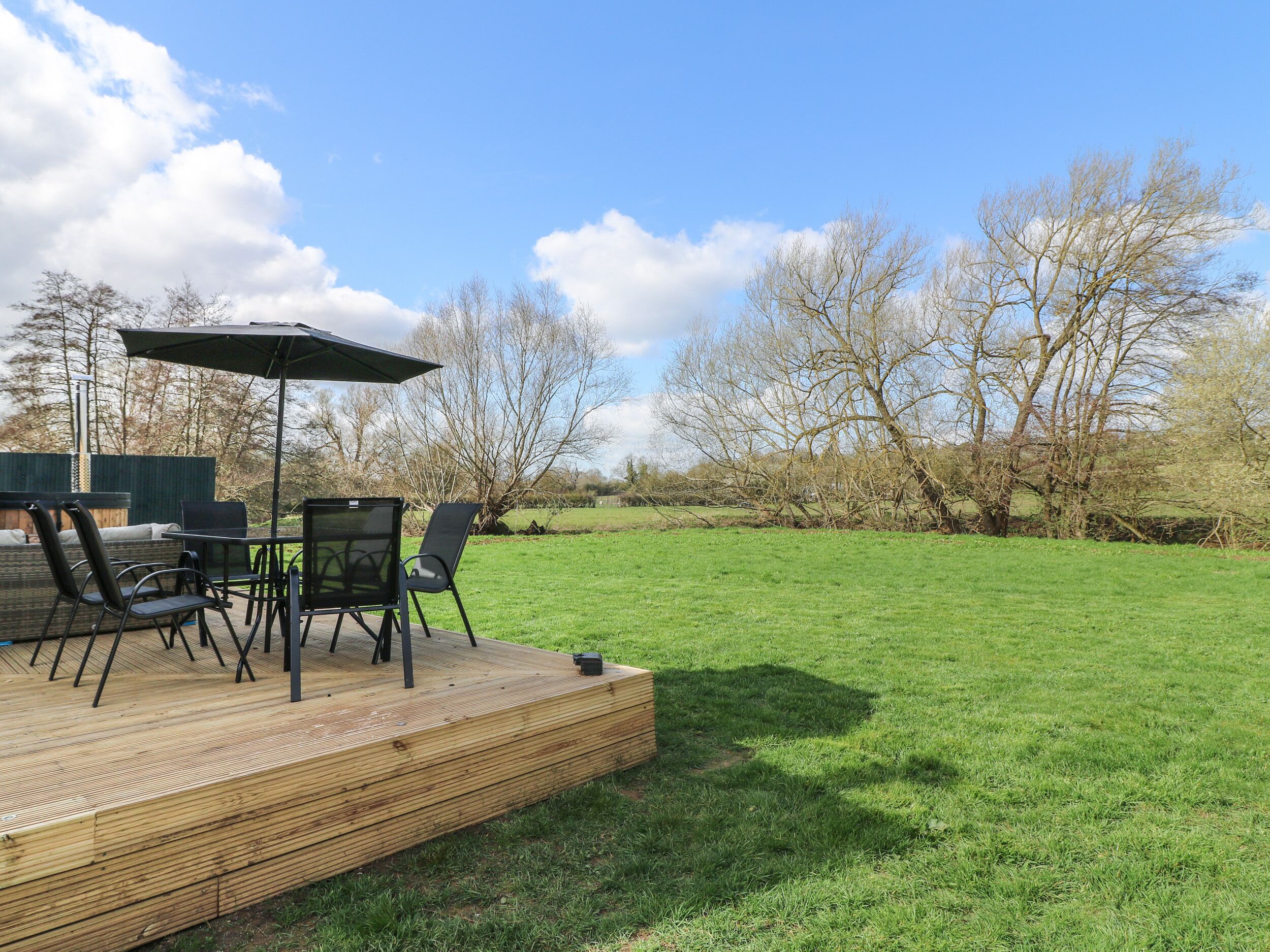 A wooden deck with outdoor furniture, including chairs and a table, overlooking a grassy area with trees.