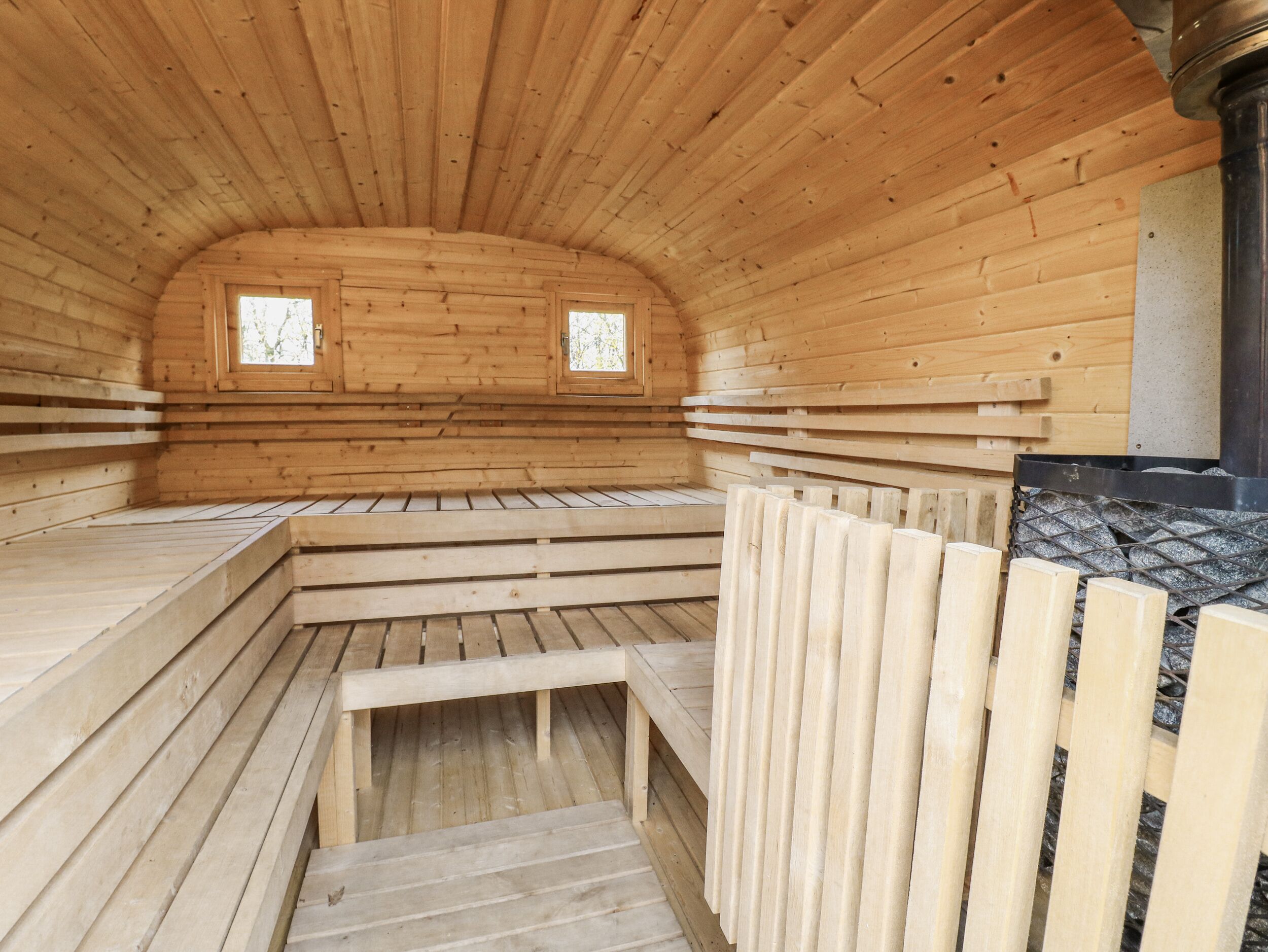 A sauna with wooden walls and benches, two windows, and a stone wall.
