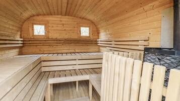 A sauna with wooden walls and benches, two windows, and a stone wall.
