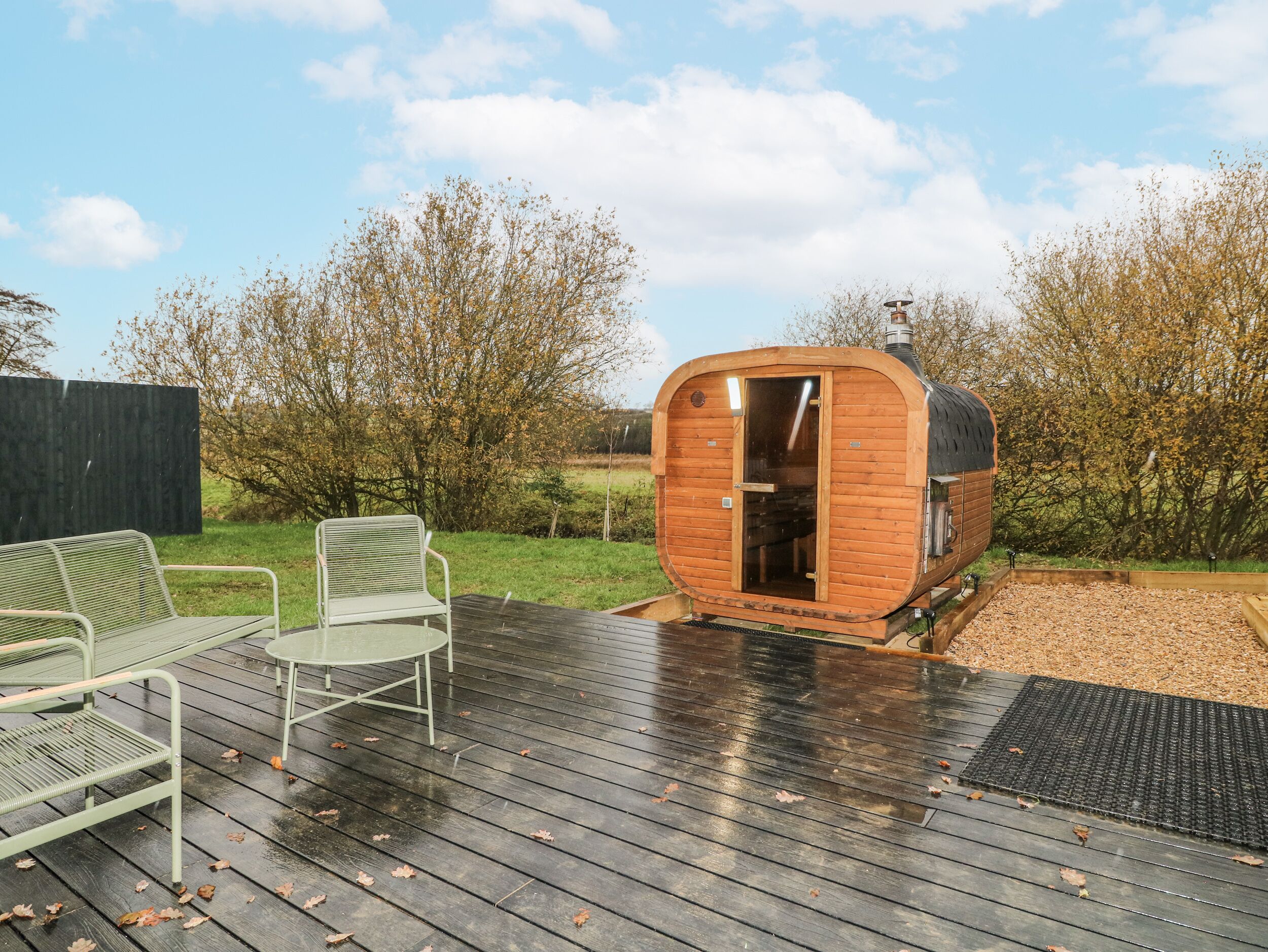 A wooden cabin with a door open, a metal chair, and a wooden deck.