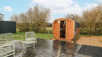 A wooden cabin with a door open, a metal chair, and a wooden deck.