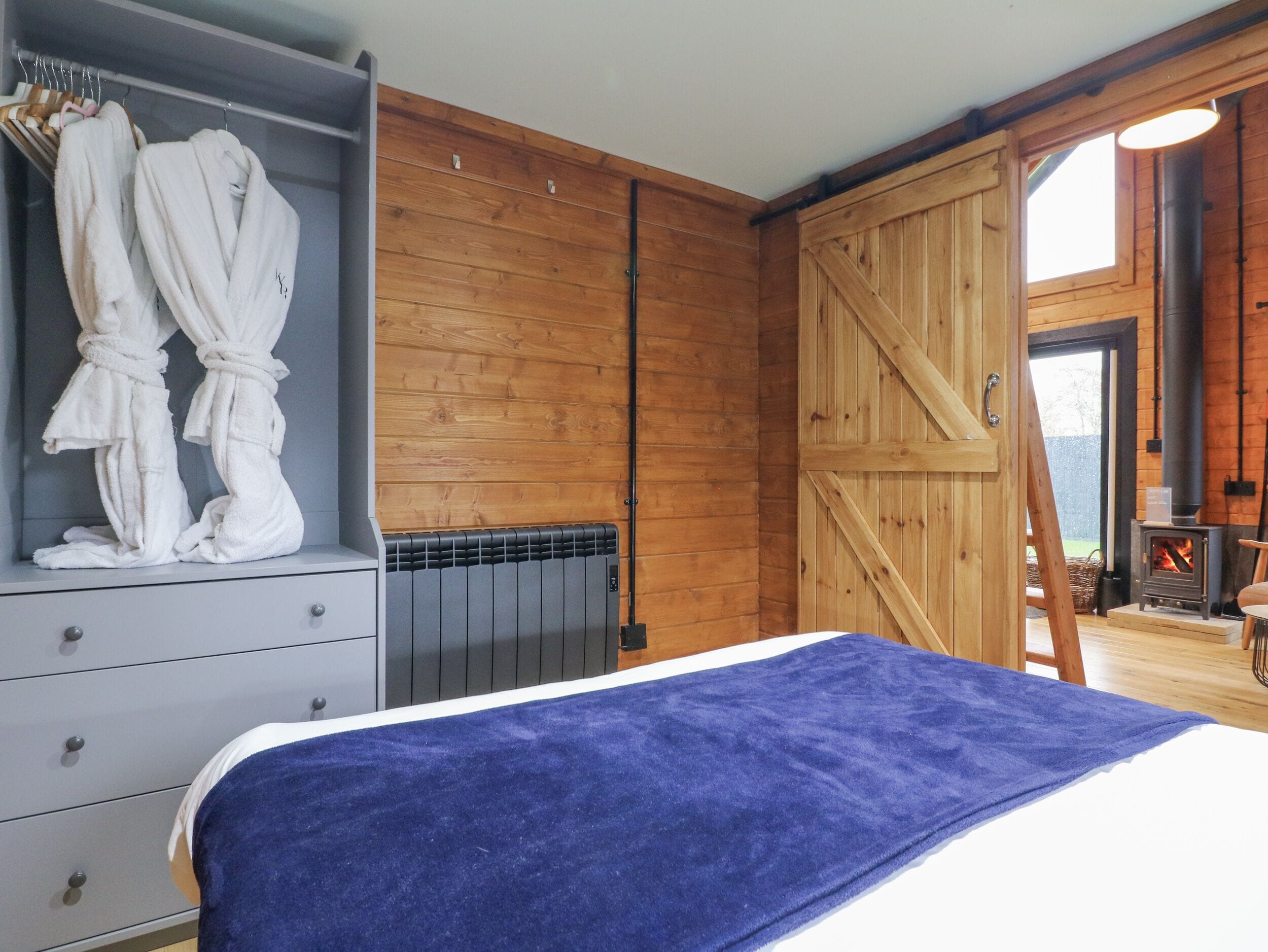 Ein Schlafzimmer mit Bett, Kleiderschrank, Heizkörper, Holzwänden und Kamin.