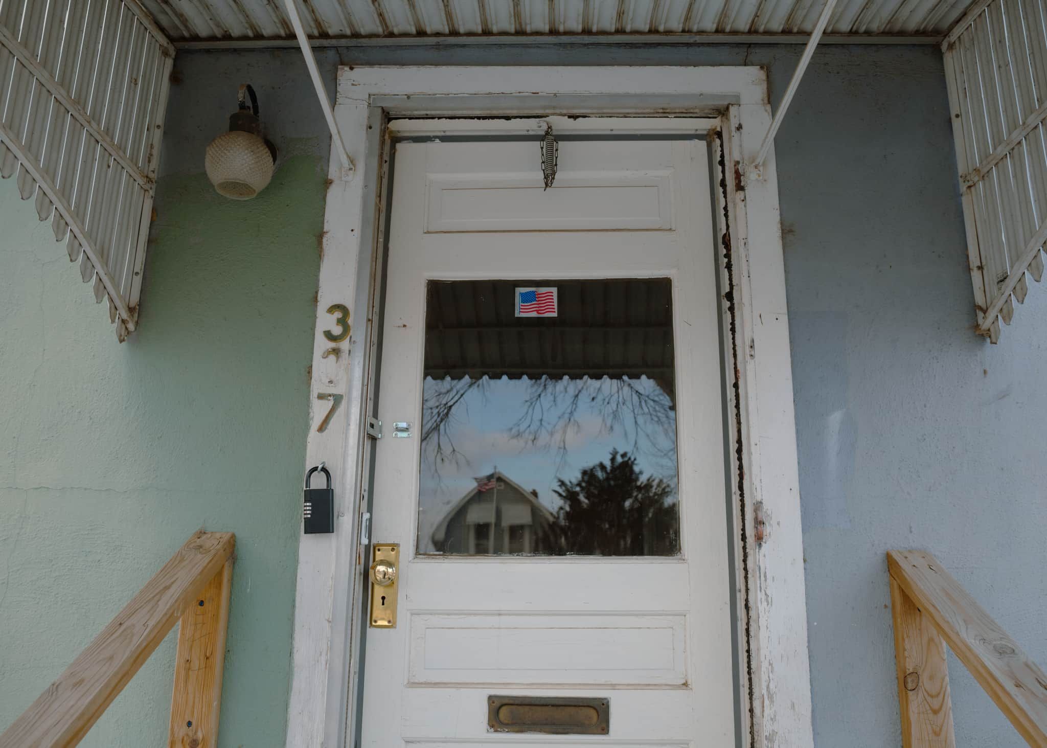 Una puerta blanca con una ventana, el número 37 en la pared y una pequeña pegatina con la bandera estadounidense.