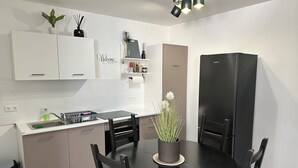 Une cuisine moderne avec des meubles blancs, une table à manger noire et un réfrigérateur noir.