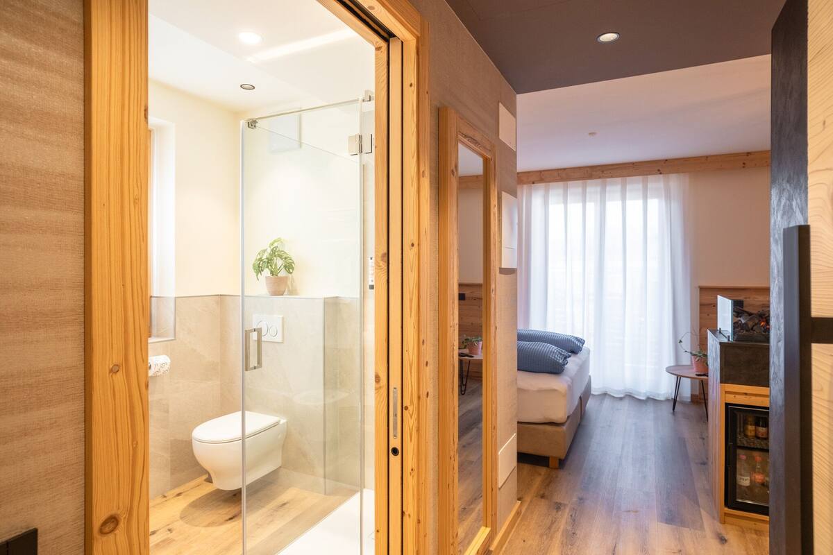 Un baño moderno con cabina de ducha de vidrio, suelo de madera y un inodoro a la vista.