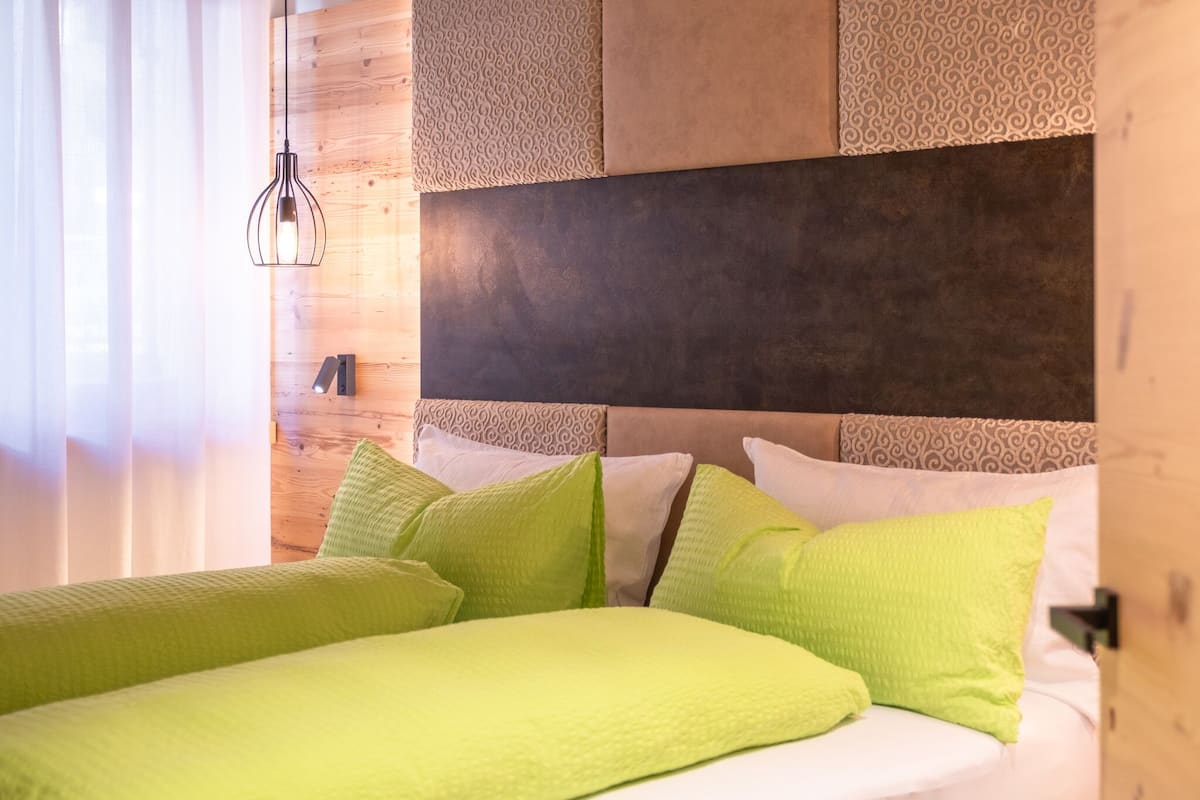 Habitación de hotel con cabecera de madera, almohadas verdes y blancas, y una lámpara colgante.