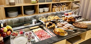 Un buffet proposant une variété de plats, notamment des pâtisseries, des fruits et des viandes.