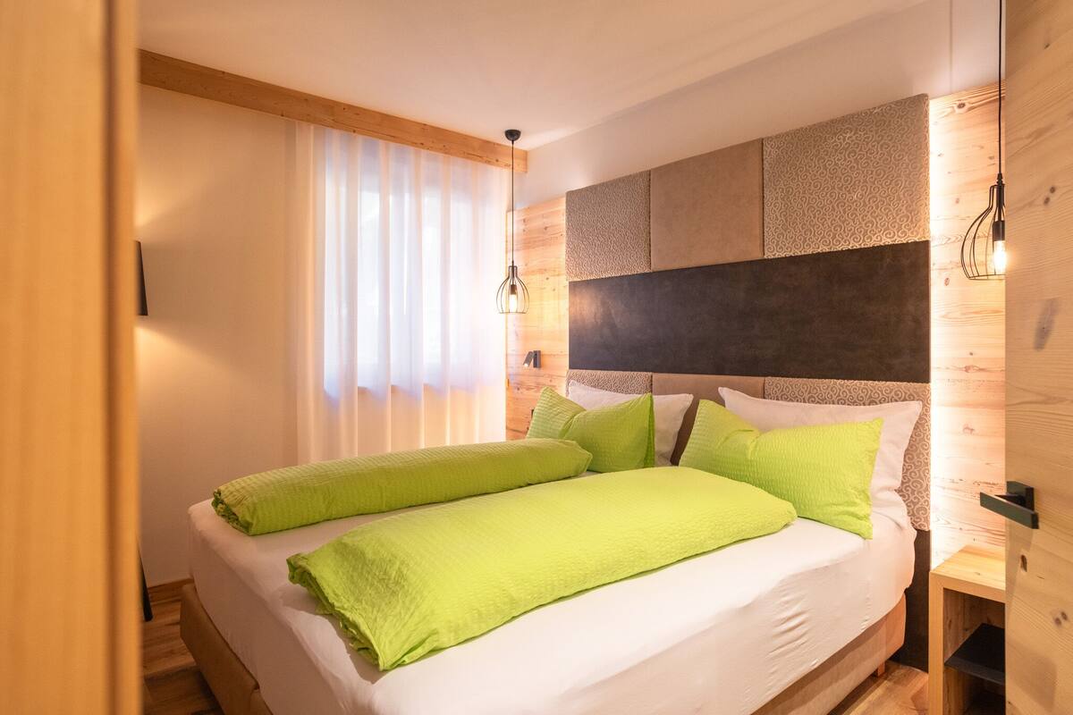 Un dormitorio con una cama grande, cabecera de madera y una ventana con cortinas de encaje.