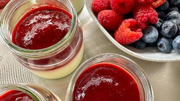 Une table avec des pots de confiture de fruits rouges, un bol de framboises et un bol de fraises.