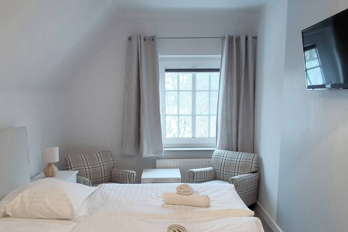 A hotel room with two beds, a TV, a window with curtains, and a radiator.