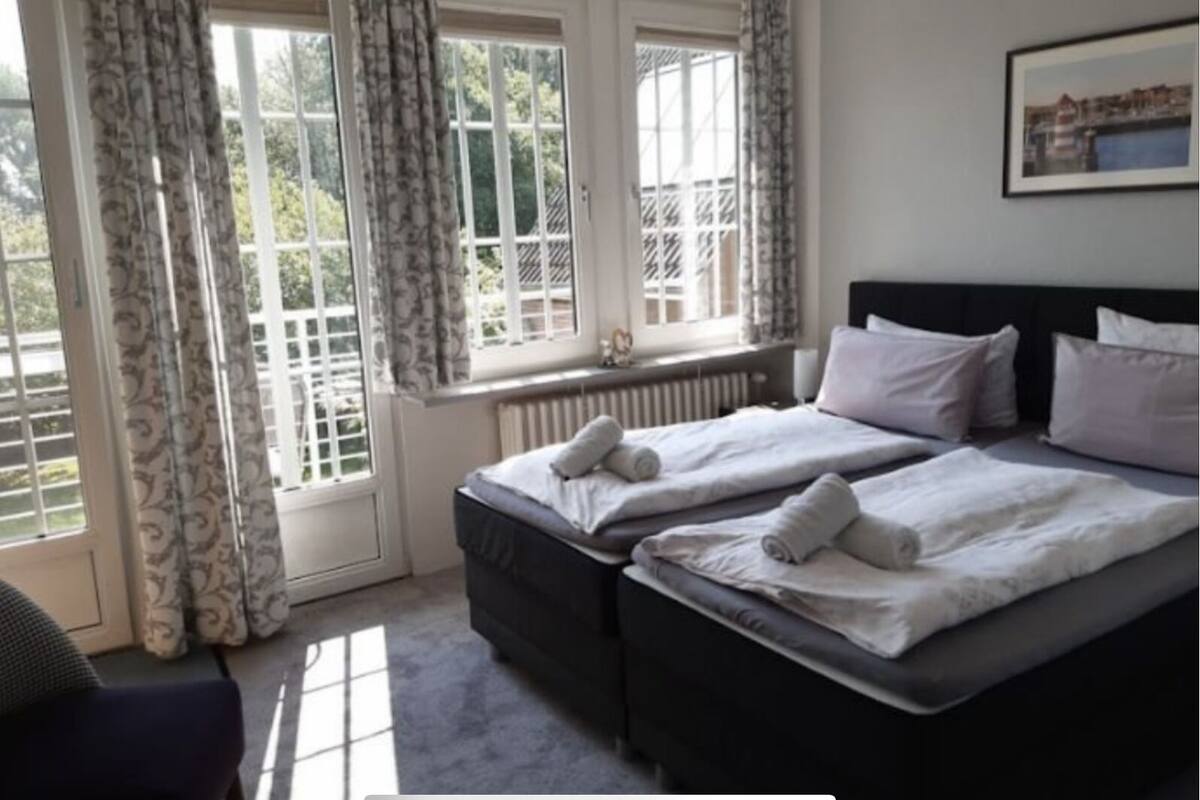 A bedroom with two beds, a radiator, and a window with curtains.