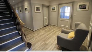 A hallway with a wooden floor, a staircase, and a gray armchair with a yellow pillow. - Pension Nordwind (Hedwigenkoog)