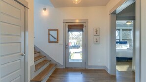 A hallway with a wooden staircase leading to a door with a window. There are framed pictures on the wall and a light fixture above the door. - Cleveland Park Charmer | Large Private Backyard (Nashville)