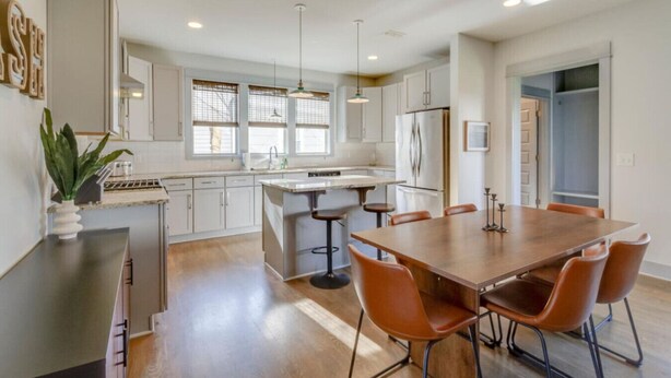 A modern kitchen with white cabinets, a central island, and a dining area with a wooden table and chairs. - Cleveland Park Charmer | Large Private Backyard (Nashville)