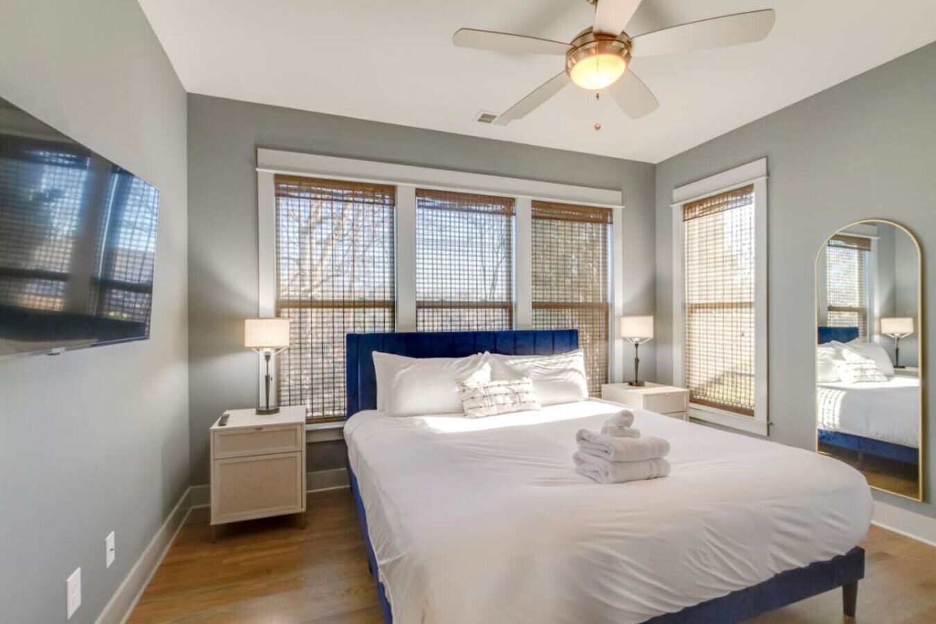 Une chambre avec un grand lit, deux tables de chevet, un ventilateur de plafond et un grand miroir.