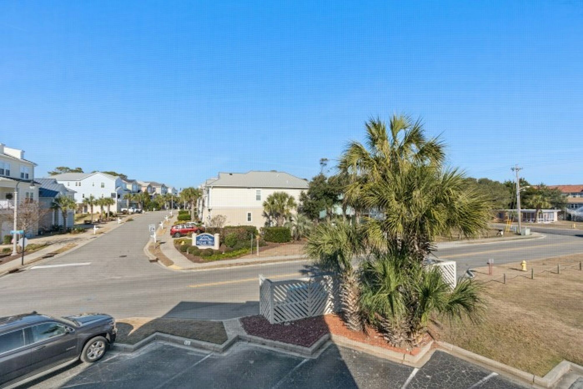 A residential street with houses, a palm tree, and a parking lot.