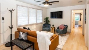 A living room with a sofa, a coffee table, a TV, a coat rack, and a plant. - Family & Dog Friendly Fun New Renovation w/ Pool!
 (Savannah)