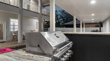 A modern outdoor kitchen with a built-in grill, a dining area with chairs, and a view of the surrounding landscape.