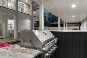 Una cocina exterior moderna con una parrilla empotrada, un comedor con sillas y vistas del paisaje circundante.