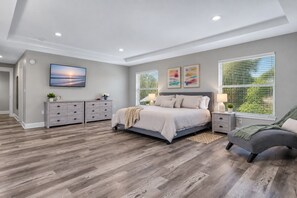 Un dormitorio con una cama grande, un aparador, una silla y dos ventanas con persianas.