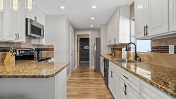 A modern kitchen with white cabinets, granite countertops, and stainless steel appliances.