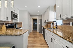 Una cocina moderna con gabinetes blancos, encimeras de granito y electrodomésticos de acero inoxidable.