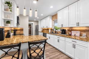 Una cocina moderna con armarios blancos, encimeras de granito e iluminación colgante.