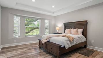 A bedroom with a large bed, a nightstand, and a window with blinds.