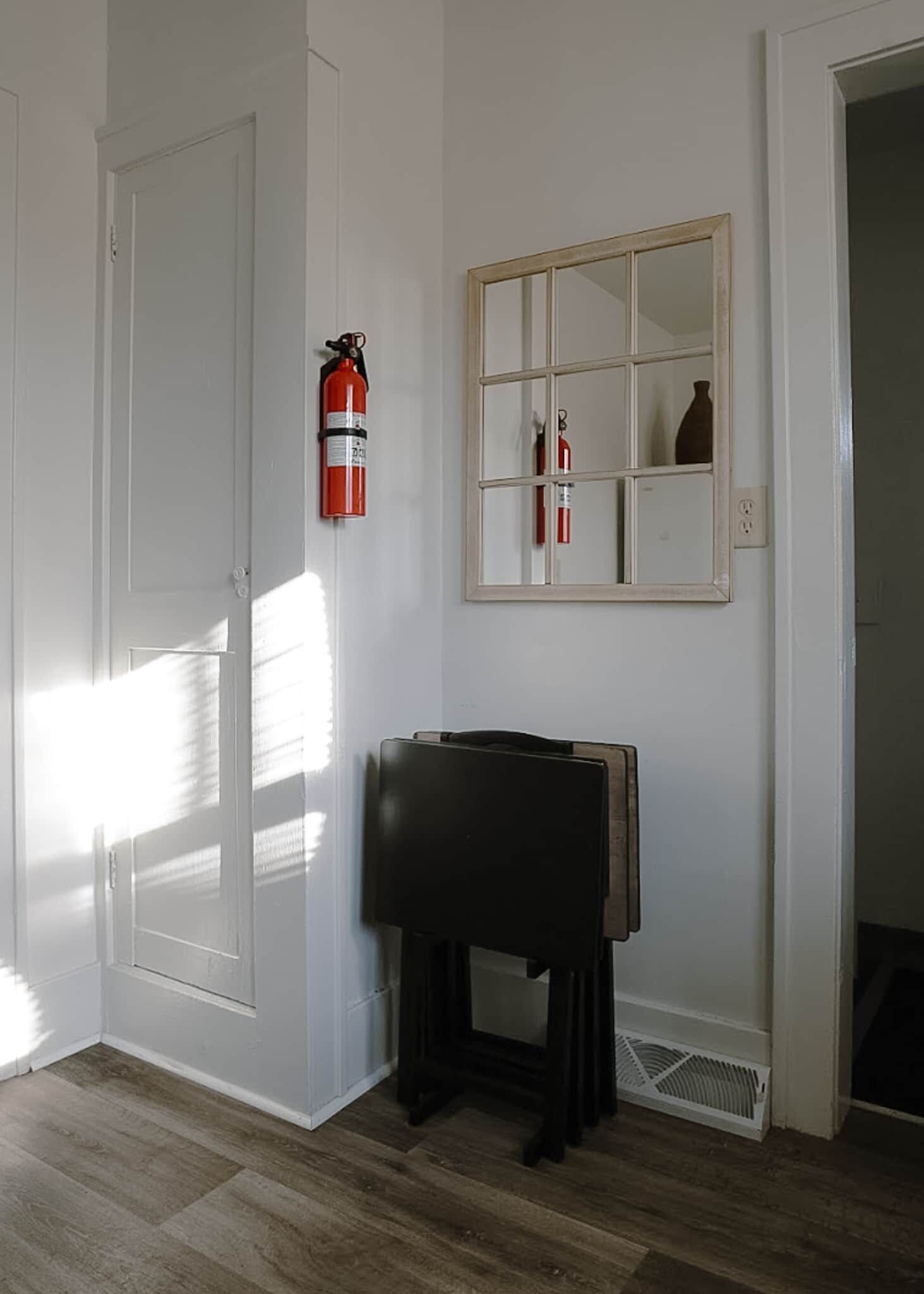 A room with a door, a fire extinguisher, a mirror, and a small table.