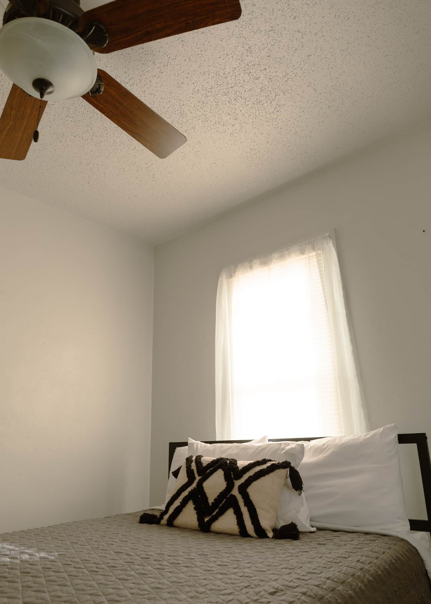 A bedroom with a bed, a ceiling fan, and a window with curtains.