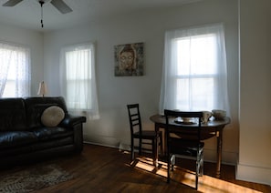 A living room with a black leather sofa, a round wooden dining table with chairs, and a ceiling fan.