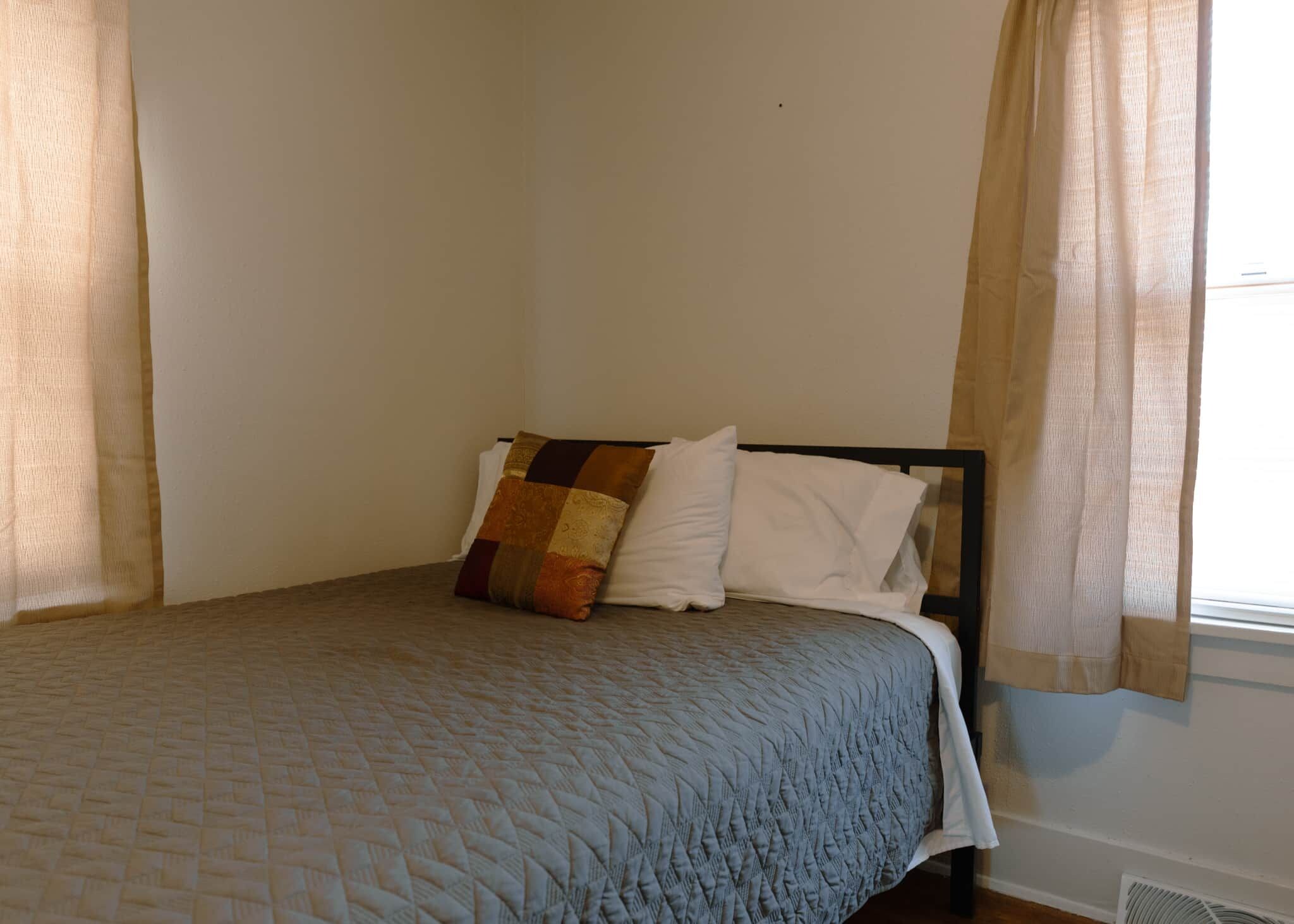 A single bed with a quilted bedspread and two pillows, one with a patterned design.