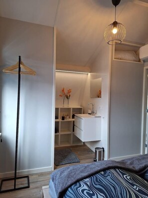 A modern bedroom with a bed, a bedside table, a hanging light fixture, and a wardrobe.