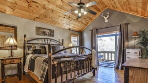 Un dormitorio rústico con una cama de madera, ventilador de techo, un escritorio de madera y un balcón con vistas.