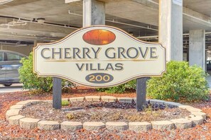 A sign for Cherry Grove Villas, number 200, with a decorative design and a sunset in the background.