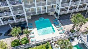 An aerial view of a hotel with a central swimming pool surrounded by lounge chairs and palm trees.