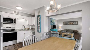 A modern kitchen with built-in appliances, a dining area with a wooden table and chairs, and a living room with a sofa and a TV.
