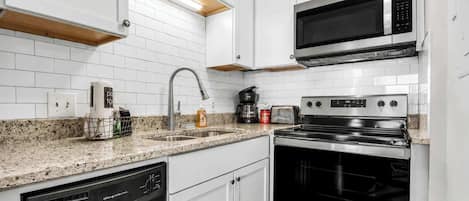 Una cocina moderna con armarios blancos, lavavajillas de acero inoxidable, horno doble y microondas.