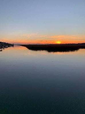 Ruhige Wasserfläche, die einen Sonnenuntergang widerspiegelt, mit einer entfernten Küstenlinie.