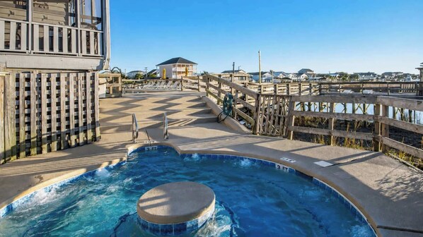 A pool area with a hot tub, wooden deck, and a view of the beach.